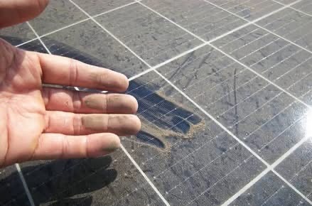 Hand wiped across a solar panel showing thick dust and grime build-up