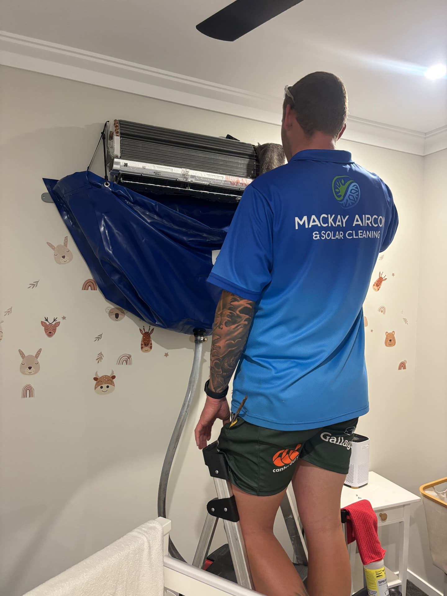 Technician pressure washing an air conditioner into a catch bag inside a Mackay home
