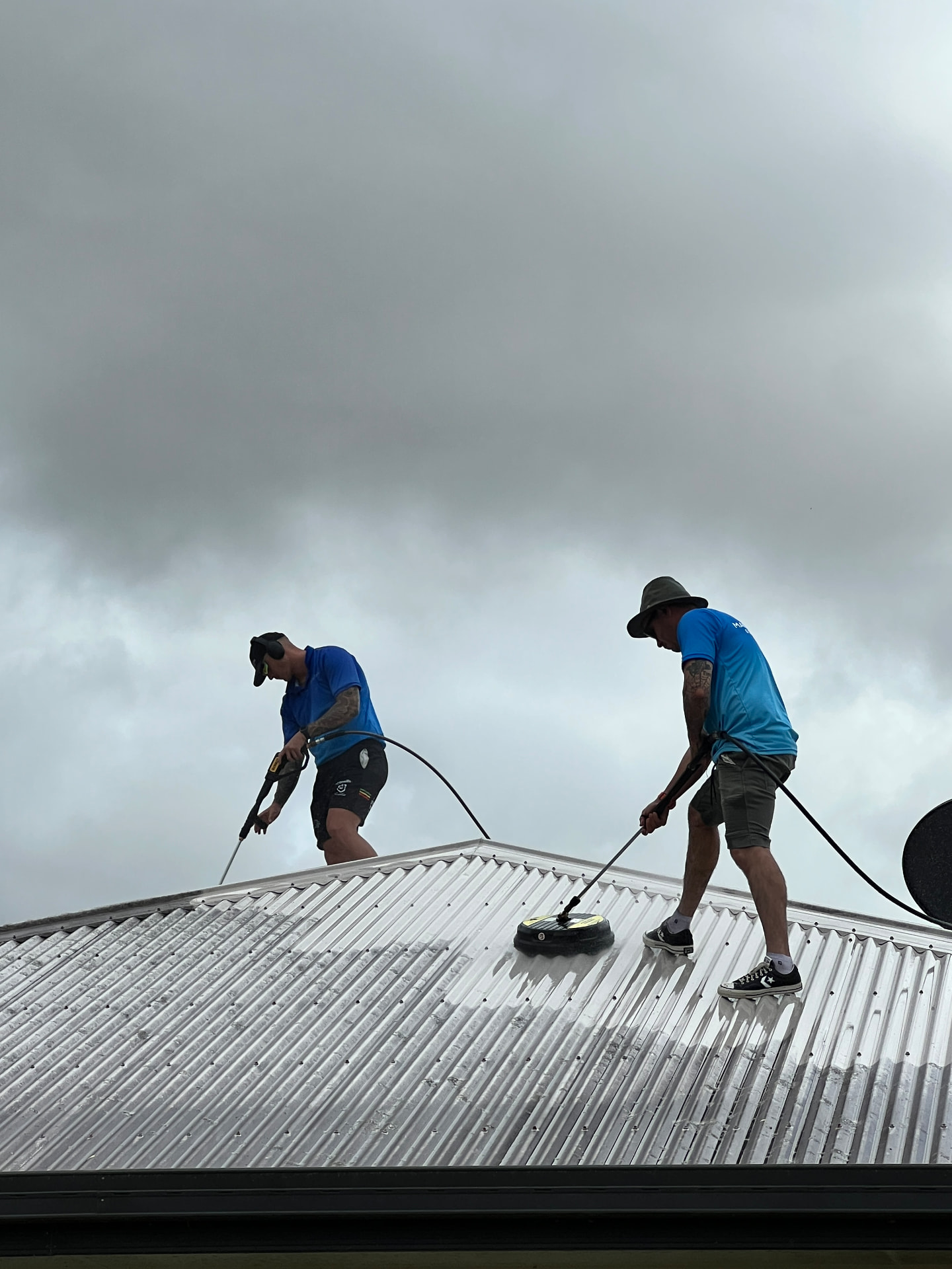 Two Mackay Aircon & Solar Cleaning technicians pressure cleaning a metal roof