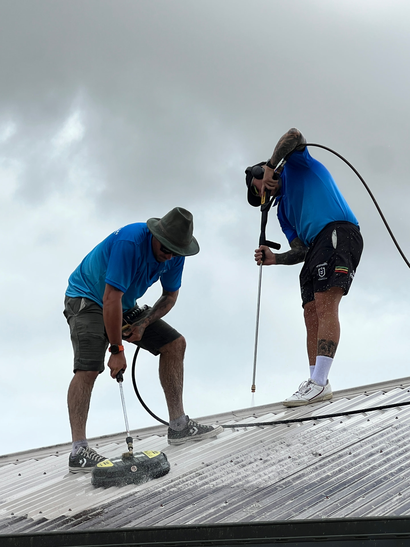 Two technicians washing a large metal roof with pressure equipment