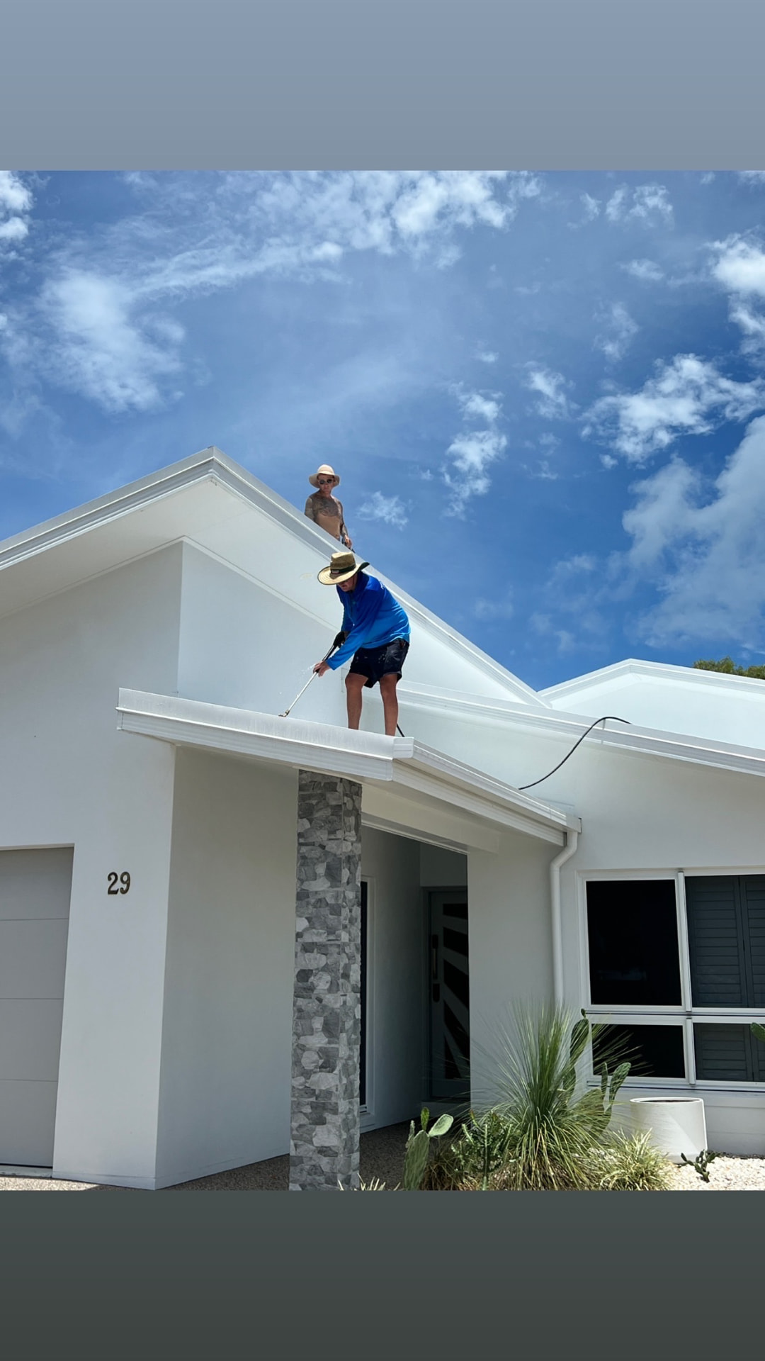Technician cleaning gutters and fascia on a white rendered home
