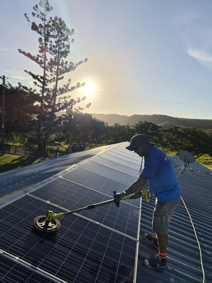 Rotary brush cleaning a rooftop solar array in morning light